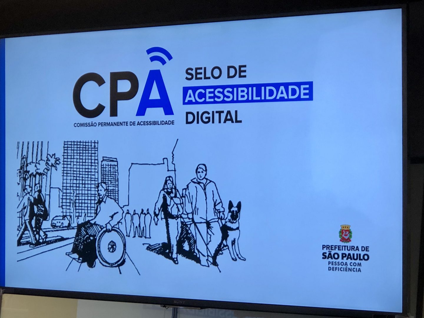 Foto com ilustração de pessoas com deficiência andando em uma calçada.