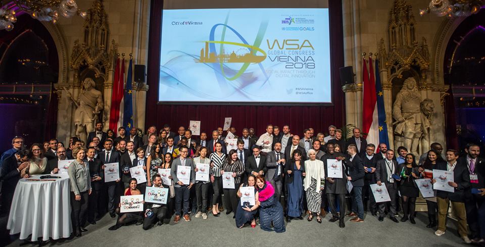 Foto de pessoas reunidas segurando diplomas. Ao fundo, há um telão com o texto: WSA 2018.
