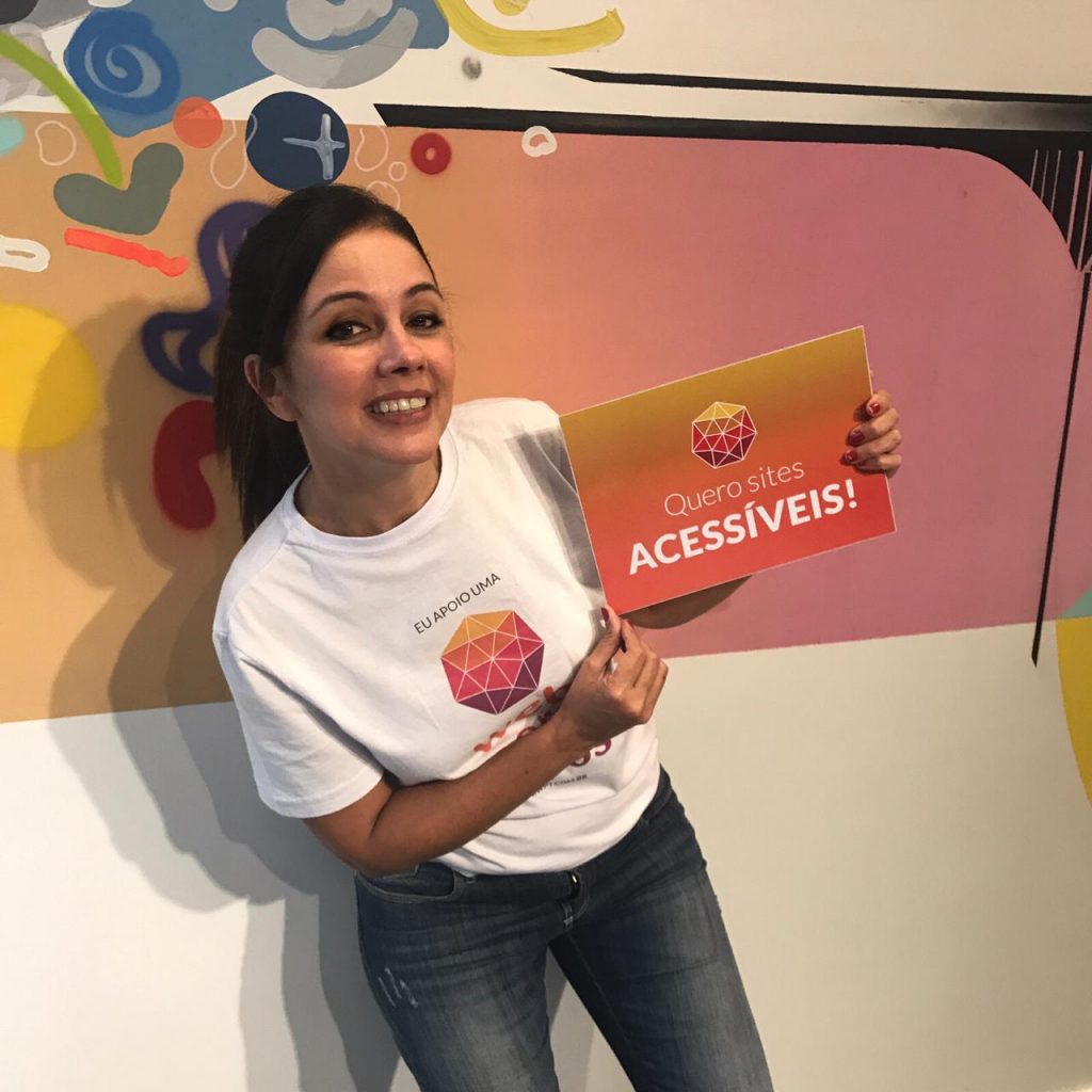 Simone Freire está em pé, sorrindo, segurando uma placa com a frase: "Quero sites acessíveis".