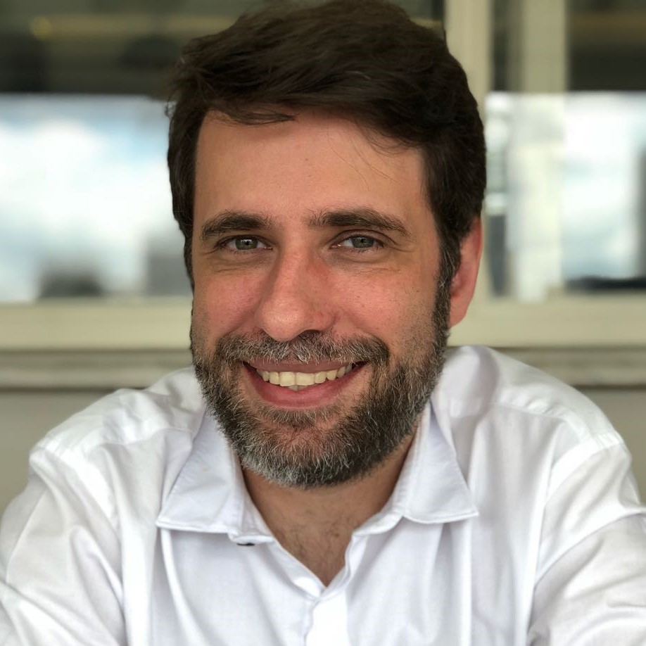 Reinaldo Ferraz está sorrindo. Ele tem cabelos curtos, barba e olhos claros.