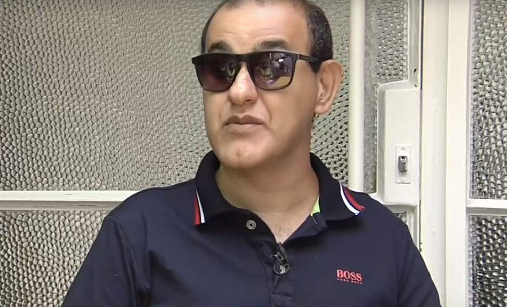 Beto Pereira está sério. Ele tem cabelos curtos, está usando óculos escuros e uma blusa azul.