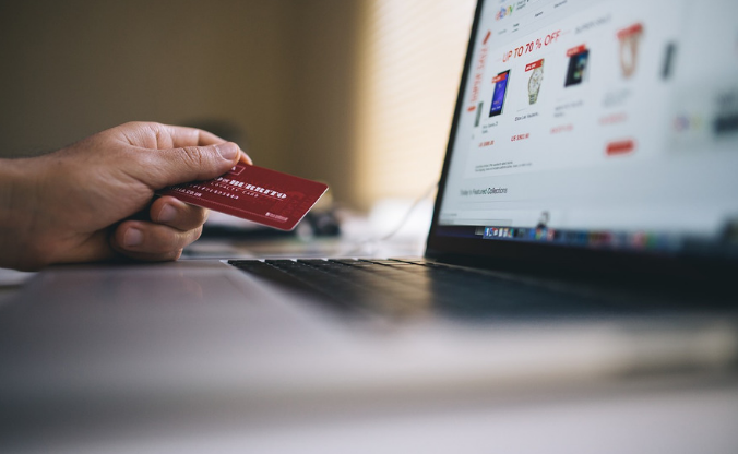 Pessoa segura cartão de crédito ao lado de um llaptop mostrando produtos na tela. 