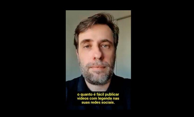 Foto da reprodução do trecho de um vídeo com Reinaldo Ferraz sério, em um ambiente fechado. No rodapé, há uma legenda amarela com fundo preto com o trecho: "o quanto é fácil publicar vídeos com legenda nas suas redes sociais". Ele tem cabelos curtos e lisos, olhos claros e barba grisalha.