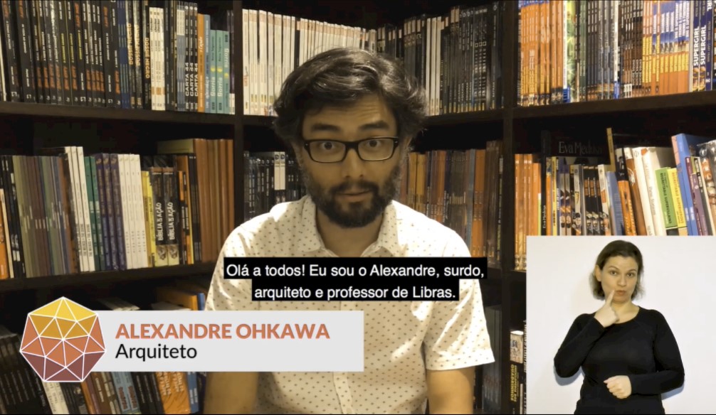 Print de tela de um vídeo do site do Web para Todos. Nele, há um homem jovem em uma sala e atrás dele há muitos livros em prateleiras. Abaixo do rosto dele está projetada uma legenda com fundo preto e o texto em branco "Olá a todos! Eu sou o Alexandre, surdo, arquiteto e professor de Libras". No rodapé à esquerda, há o logo do Web para Todos e o texto "Alexandre Ohkawa, arquiteto". No canto inferior direito, há uma intérprete de Libras em janela com fundo branco.