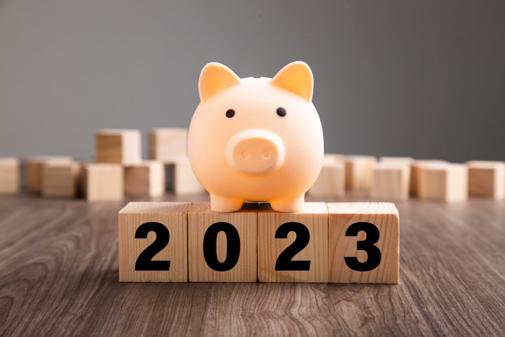 Foto de um cofrinho para moedas em formato de porquinho. Ele está sobre cubos de madeira que formam juntos o número 2023.