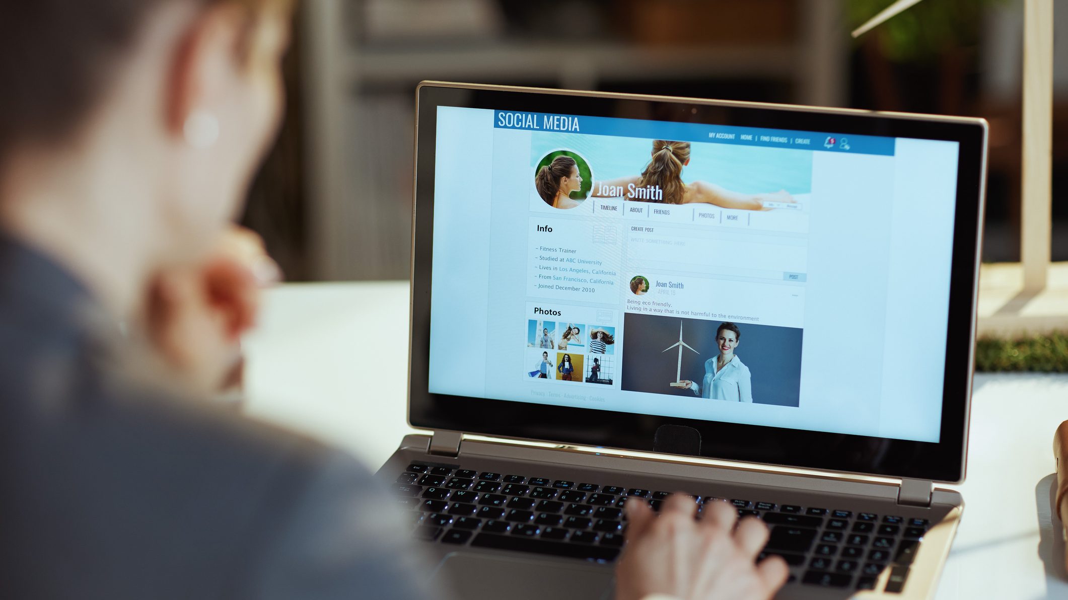 Foto de pessoa desfocada de frente a um notebook com uma rede social projetada na tela.